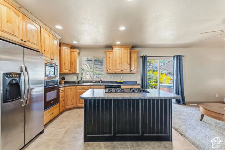 Kitchen featuring wood cabinetry, stainless steel appliances, a center island with a cooktop, and a sliding glass door