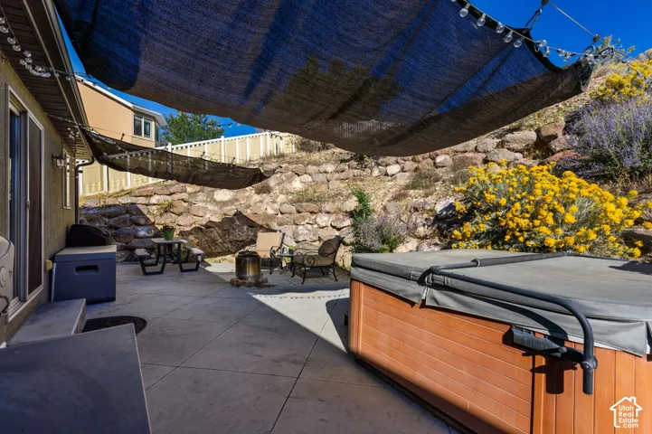 Spacious patio featuring a hot tub, string lights, and a rock retaining wall