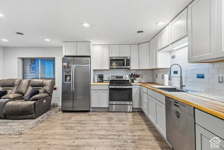 Kitchen featuring wood-finish flooring, shaker-style cabinetry, wood countertops, a stainless steel appliance suite, and a subway tile backsplash