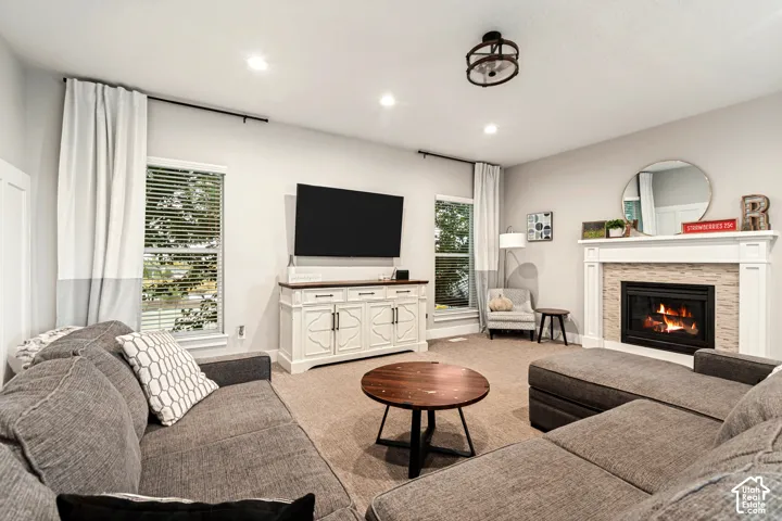 Recessed lighting, a fireplace with a stacked stone surround and white mantel, a ceiling-mounted light fixture, and windows with horizontal blinds