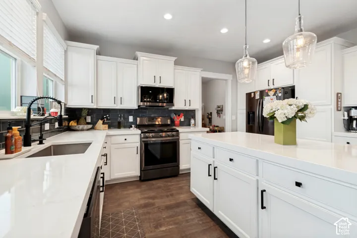 White shaker cabinetry with dark hardware, quartz countertops, stainless steel appliances, dark subway tile backsplash, and wood-finish flooring