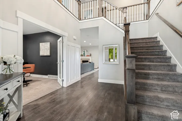 Wood-finish flooring, staircase with carpeted treads, white paneling, and a two-story entryway