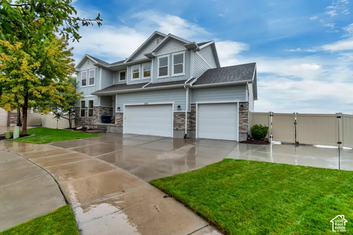 Light blue siding exterior with stone accents, featuring a two-car garage, a single-car garage, a paved driveway, and a fenced yard