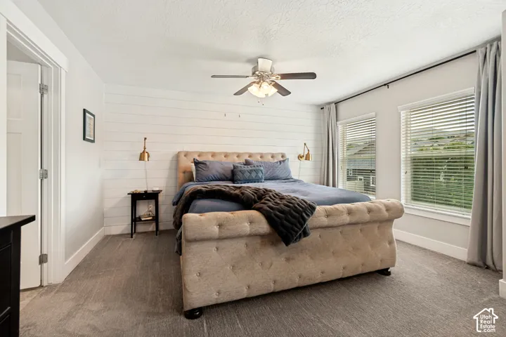 Carpeted flooring, white shiplap accent wall, ceiling fan with integrated lighting, two windows with blinds, and a solid core door
