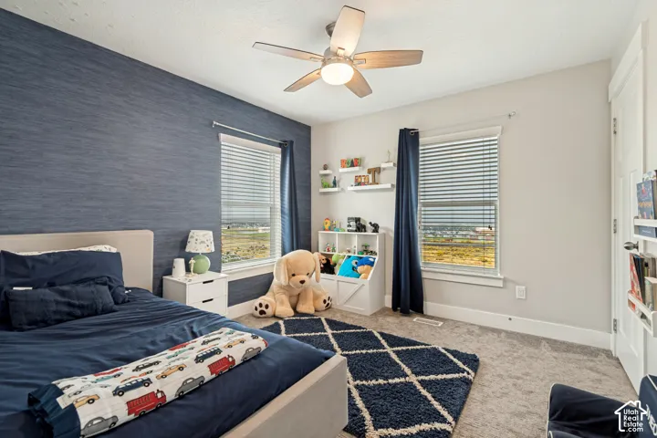 Textured accent wall, ceiling fan with integrated lighting, two windows with blinds, built-in shelving, and carpeted flooring