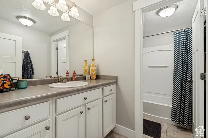 Bathroom featuring a vanity with white cabinetry, a single basin sink, a large wall-mounted mirror, overhead vanity lighting, and a shower-over-tub combination