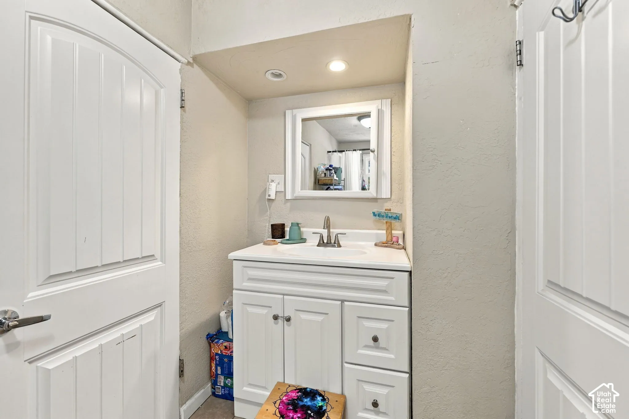 White paneled vanity with chrome hardware, integrated sink, and wall-mounted mirror