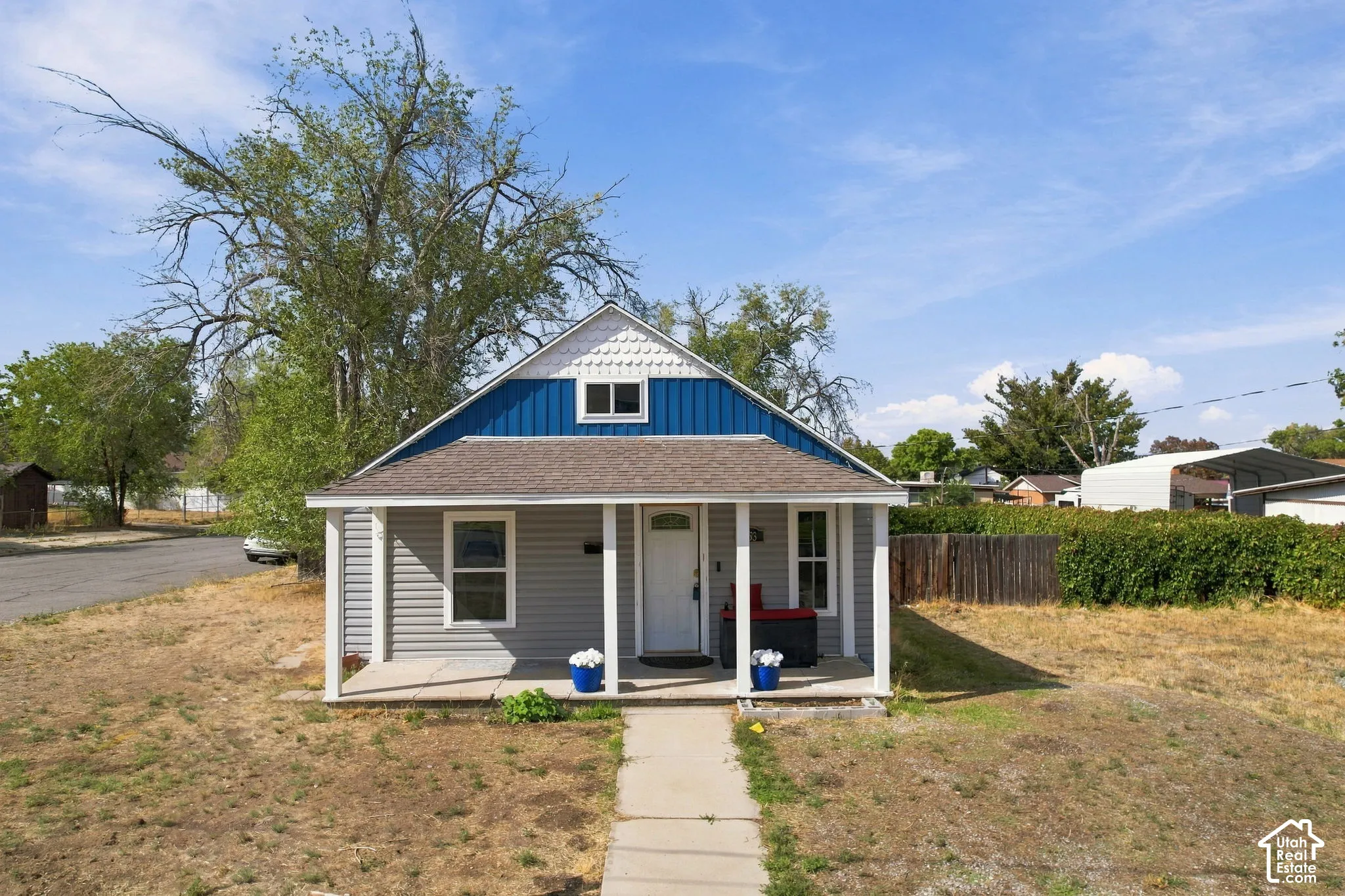 Front exterior with gray horizontal siding, blue vertical siding, a white front porch with square columns, and a gabled roof