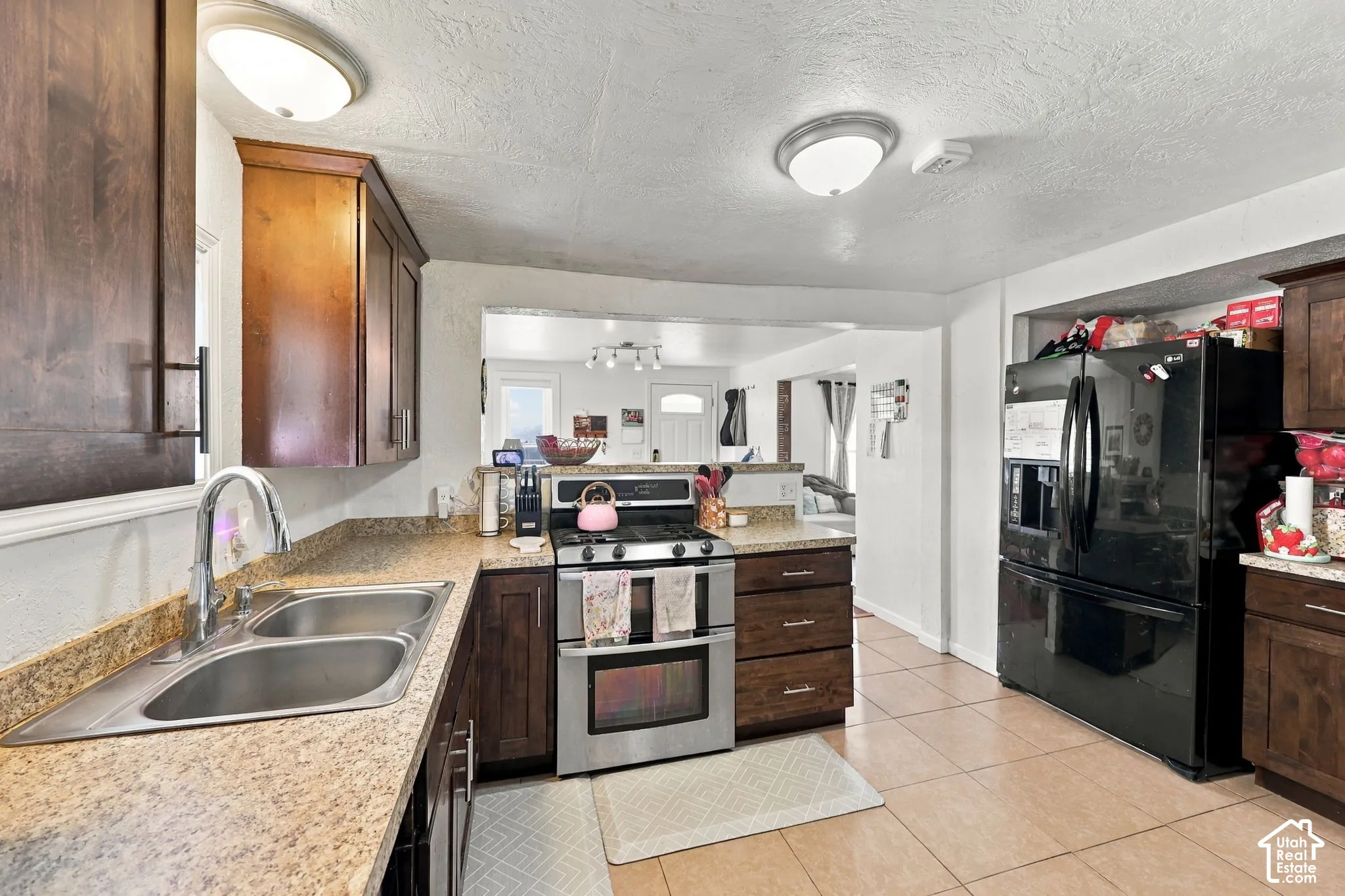 Kitchen featuring wood cabinetry, a double basin stainless steel sink, a stainless steel range with an oven, and tile flooring