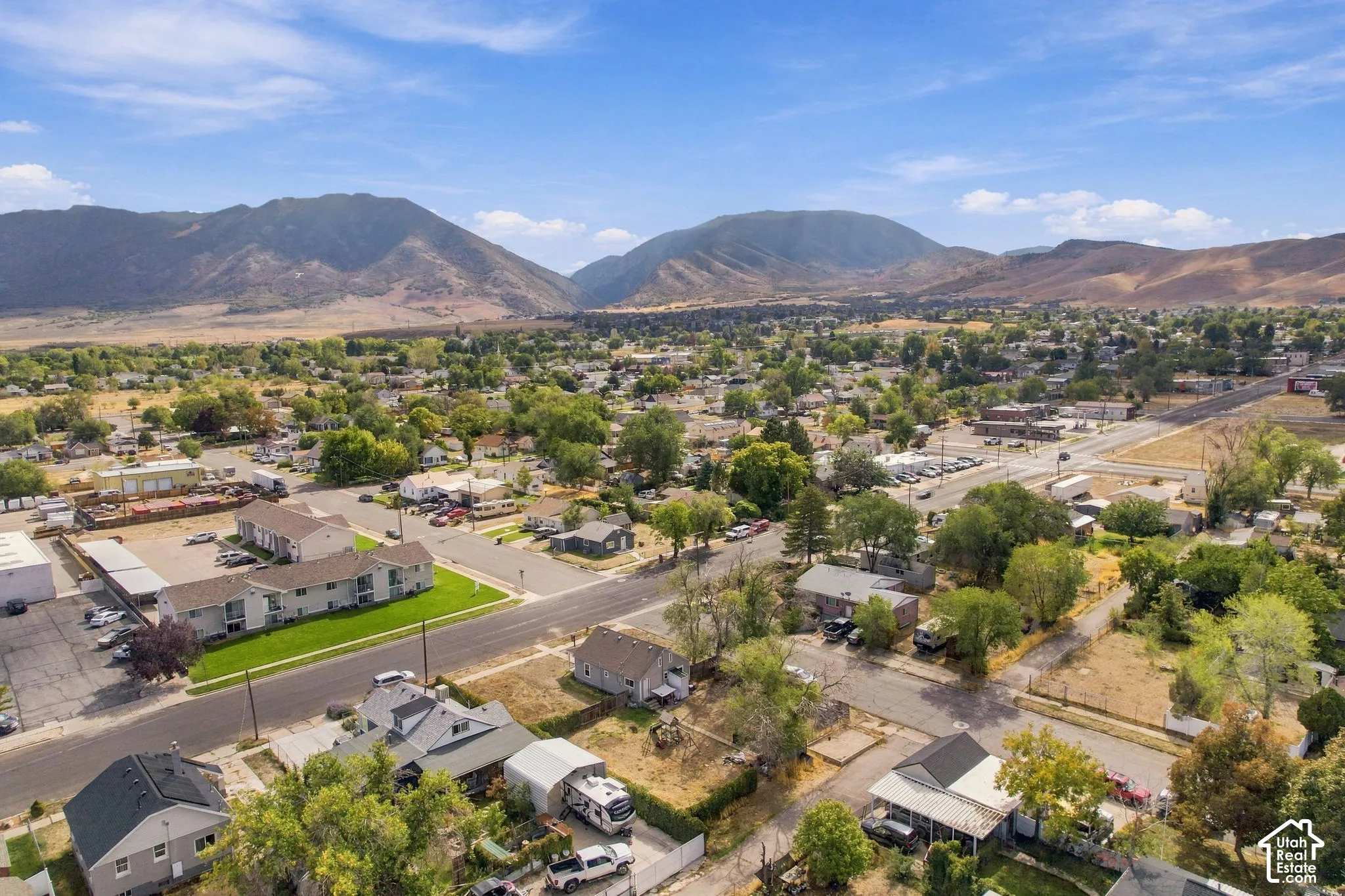 Mountainous terrain in the background, residential and commercial properties, established greenery, paved roads, and clear skies