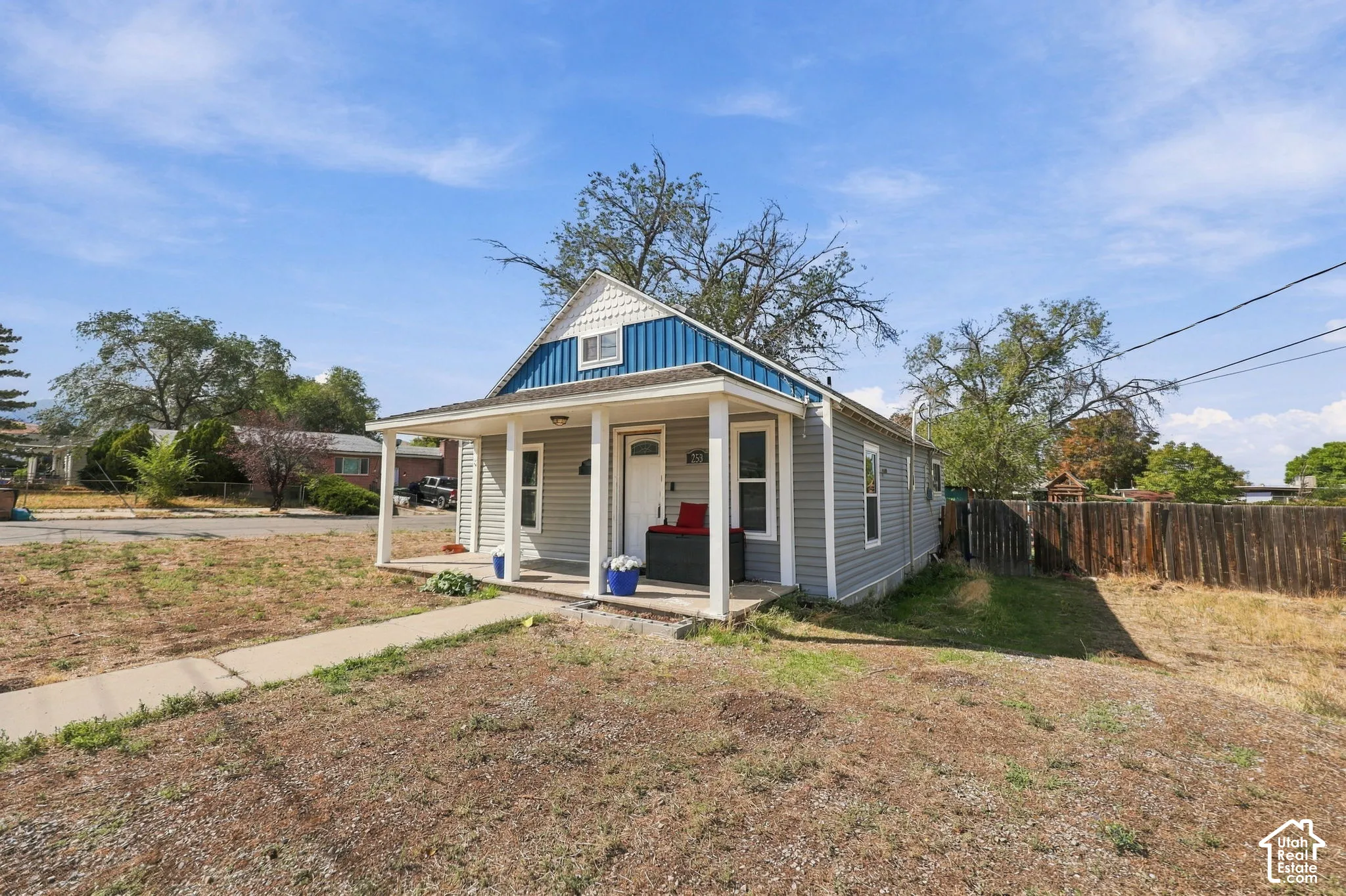 Exterior featuring gray siding, a covered porch, white columns, a blue metal roof accent, and a front walkway