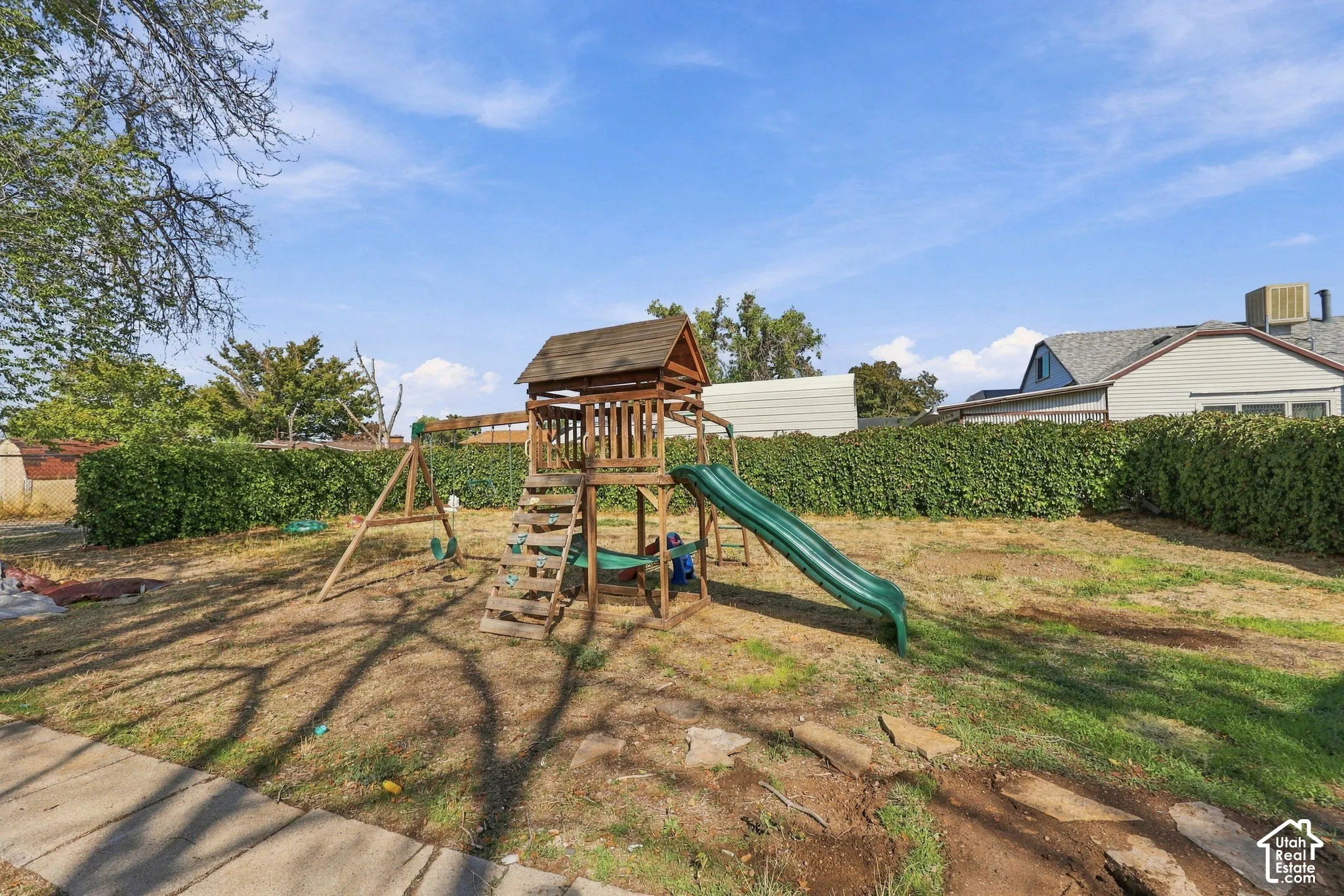 Expansive backyard with a wooden playset featuring a slide and swings