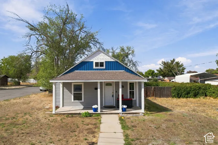 Front exterior with gray horizontal siding, blue vertical siding, a white front porch with square columns, and a gabled roof