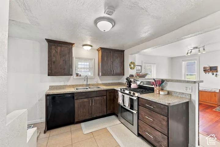 Dark wood-finish cabinetry, stainless steel oven, integrated dishwasher, light speckled countertops, and tile flooring
