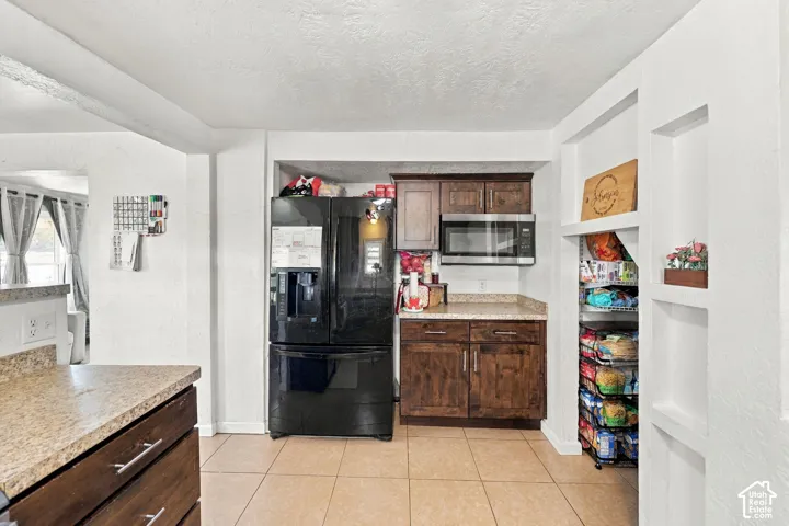 Kitchen featuring dark wood-finish cabinetry, black appliances, light-toned countertops, and tiled flooring