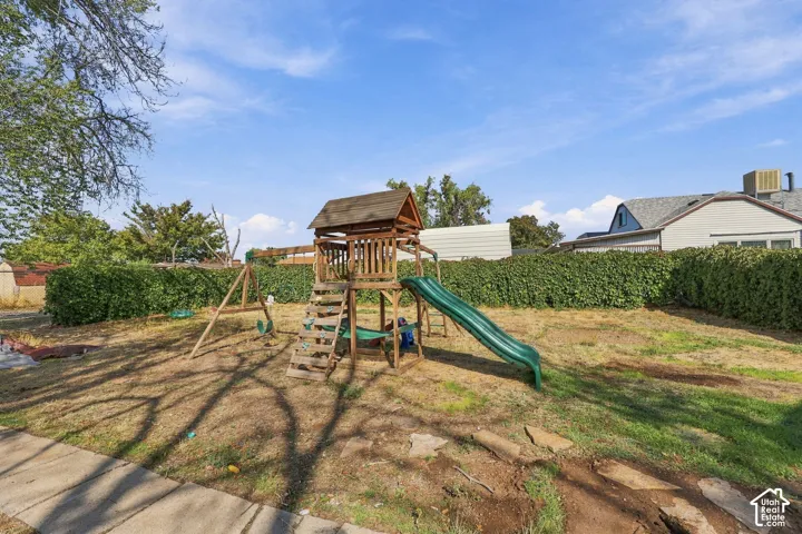 Expansive backyard with a wooden playset featuring a slide and swings