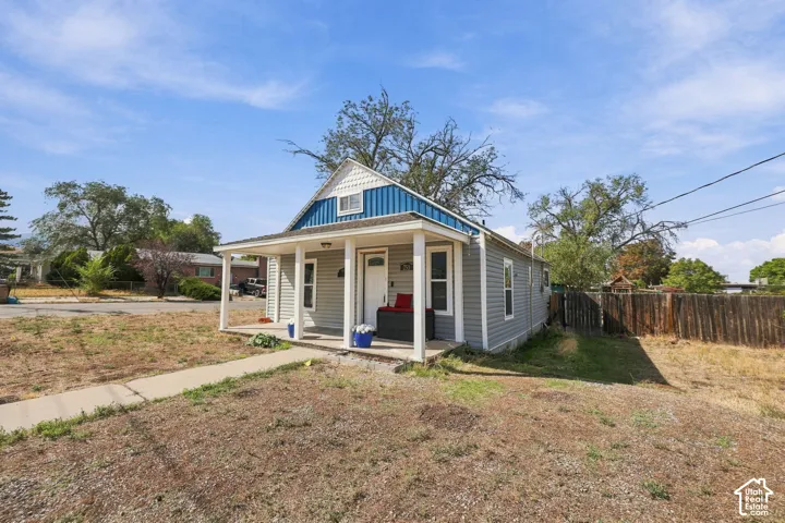 Exterior featuring gray siding, a covered porch, white columns, a blue metal roof accent, and a front walkway