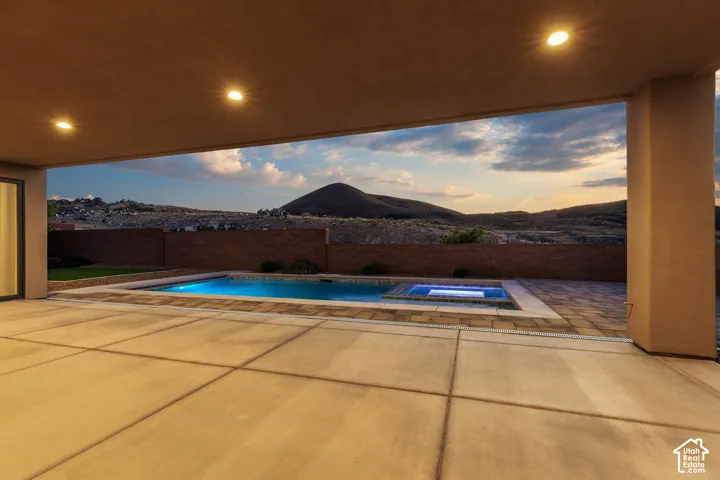 Expansive concrete patio with recessed lighting, featuring an in-ground swimming pool and integrated spa
