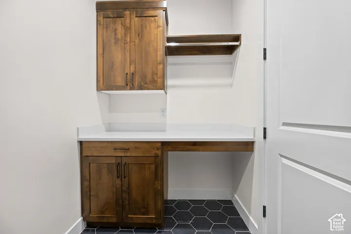 Wood-finish cabinetry with dark hardware, a white countertop, and dark hexagonal floor tiling