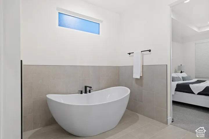 Freestanding soaking tub with matte black fixtures, tile wainscoting, and a transom window