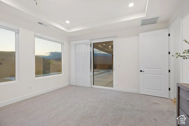 Recessed lighting, tray ceiling, grey carpeting, two large windows, and a sliding glass door