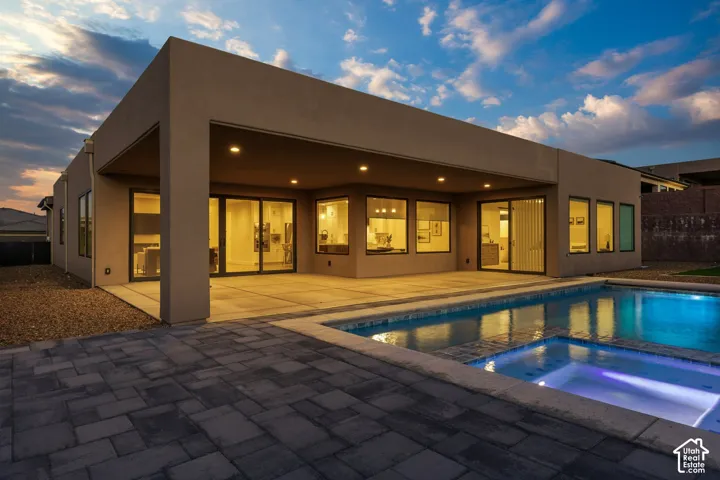 Stucco exterior with a covered patio, concrete patio, swimming pool, and paver hardscaping