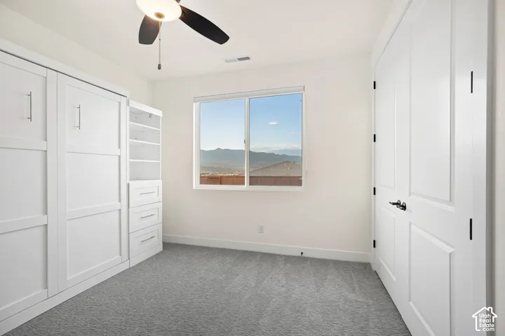 Built-in cabinetry with shelving and drawers, window with mountain backdrop, ceiling fan with integrated lighting, and carpeted flooring