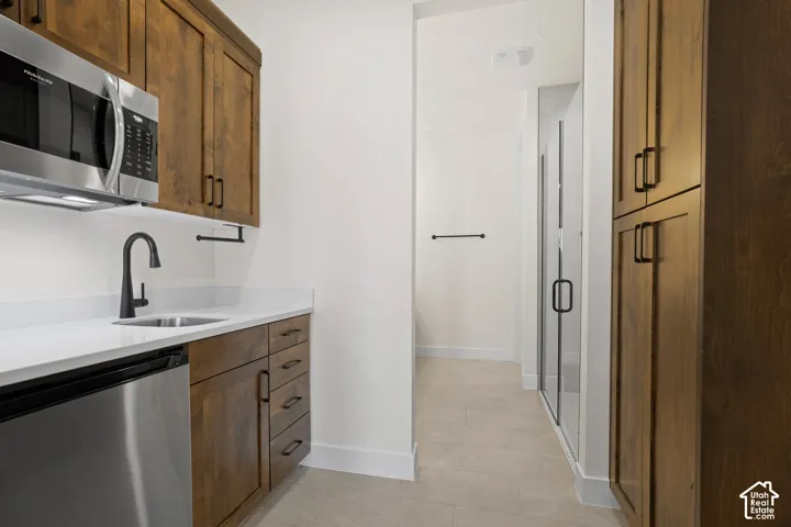 Kitchenette with wood-finish cabinetry, stainless steel microwave, stainless steel undercounter refrigerator, and white countertop
