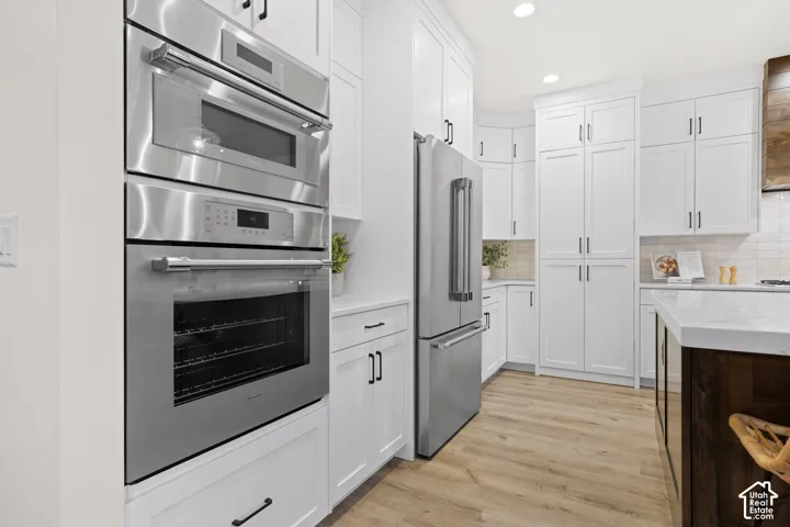 Full kitchen featuring stainless steel appliances, white cabinetry, wood-finish flooring, white subway tile backsplash, and a dark wood-finish island with a light countertop