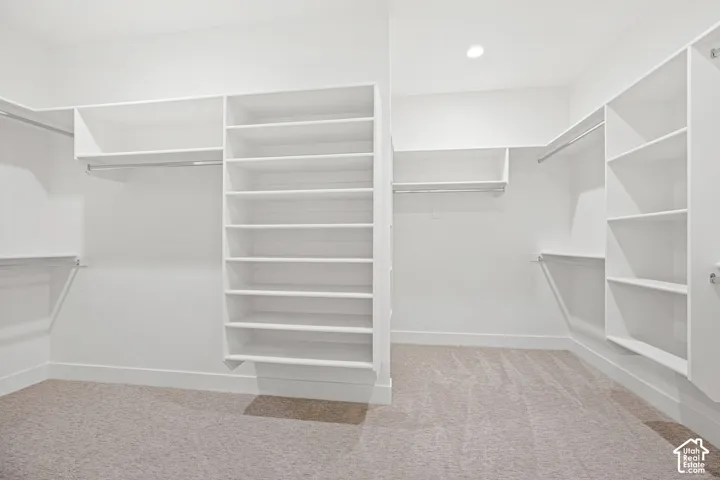Built-in shelving, white cabinetry, integrated hanging rods, recessed lighting, and carpeted flooring