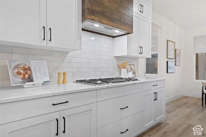 White shaker cabinetry, stone countertops, integrated gas cooktop, wood-finish flooring, and a textured subway tile backsplash