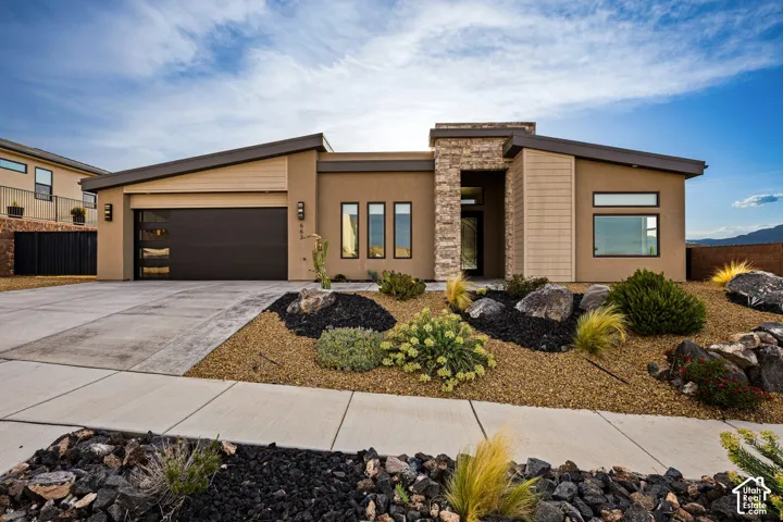 Contemporary exterior with a stone column entrance, a dark-paneled garage door, and desert-style landscaping