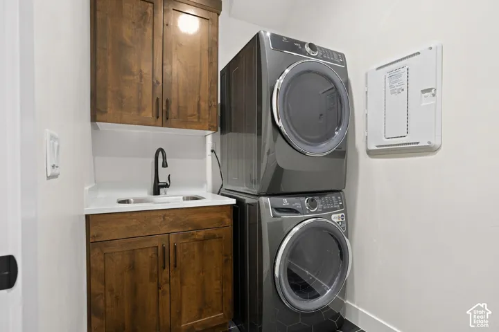 Laundry area featuring stacked washer and dryer, wood cabinetry, white countertop with undermount sink, and dark faucet