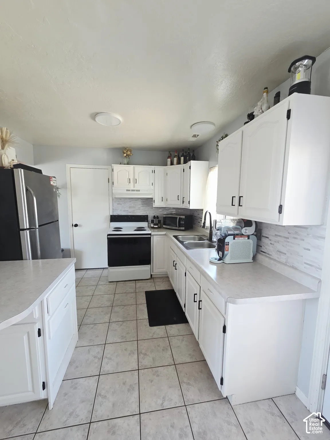 Kitchen featuring white cabinetry, tile flooring, light countertops, a stainless steel sink, and a tiled backsplash
