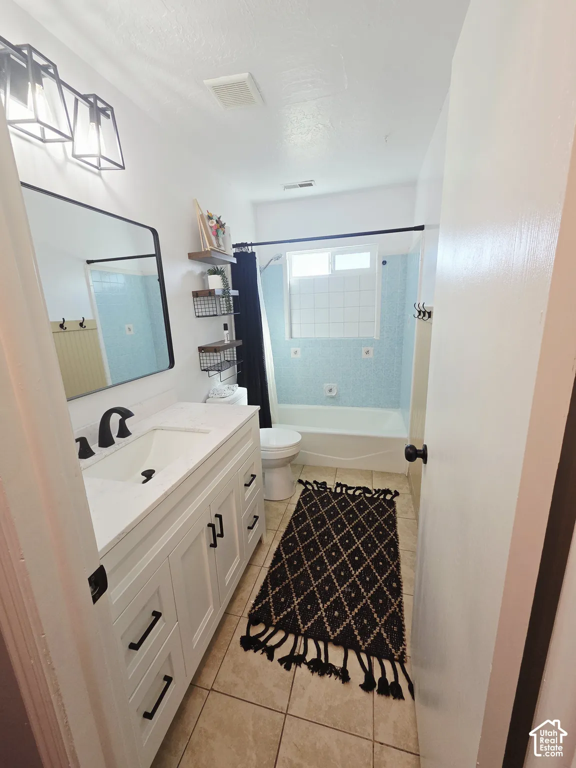Bright, renovated bathroom featuring a white vanity with ample storage and black hardware, ceramic tile flooring, a frameless glass-enclosed shower with tile surround, and recessed ceiling lighting