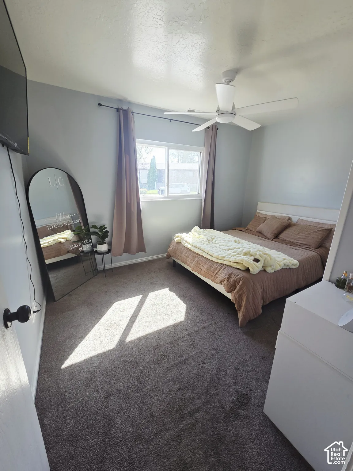 Window with curtain rods, light gray walls, dark carpet, and a ceiling fan