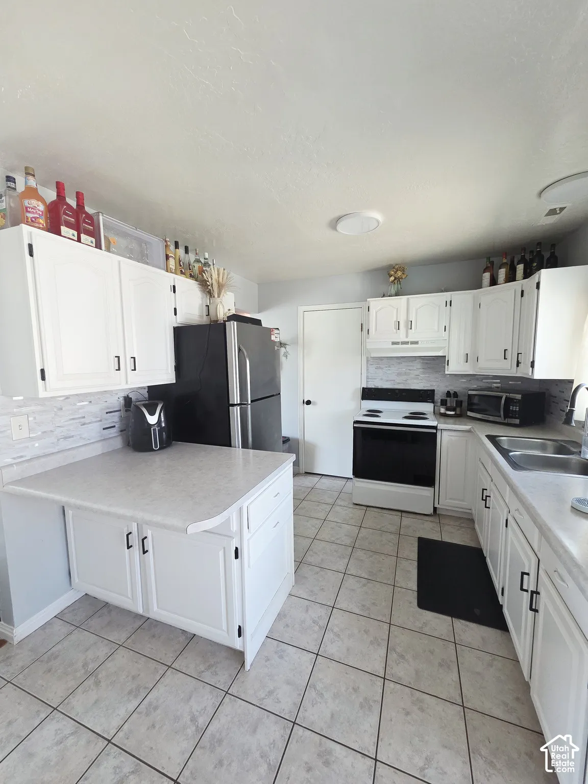 Spacious kitchen featuring white cabinetry with hardware accents, stainless steel appliances including a refrigerator and electric range, tile flooring throughout, and ample counter space with a centered island