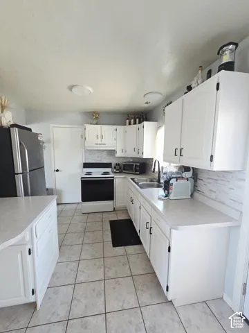 Kitchen featuring white cabinetry, tile flooring, light countertops, a stainless steel sink, and a tiled backsplash