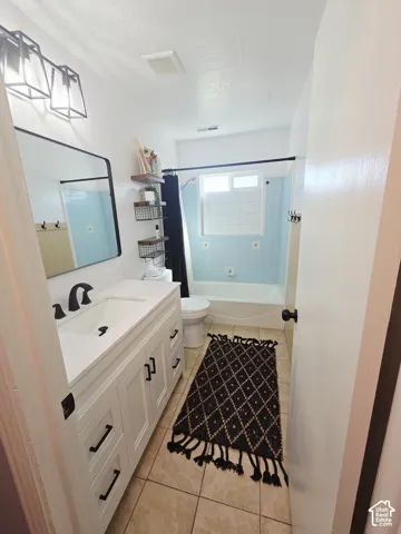 Bright, renovated bathroom featuring a white vanity with ample storage and black hardware, ceramic tile flooring, a frameless glass-enclosed shower with tile surround, and recessed ceiling lighting