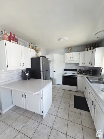 Spacious kitchen featuring white cabinetry with hardware accents, stainless steel appliances including a refrigerator and electric range, tile flooring throughout, and ample counter space with a centered island
