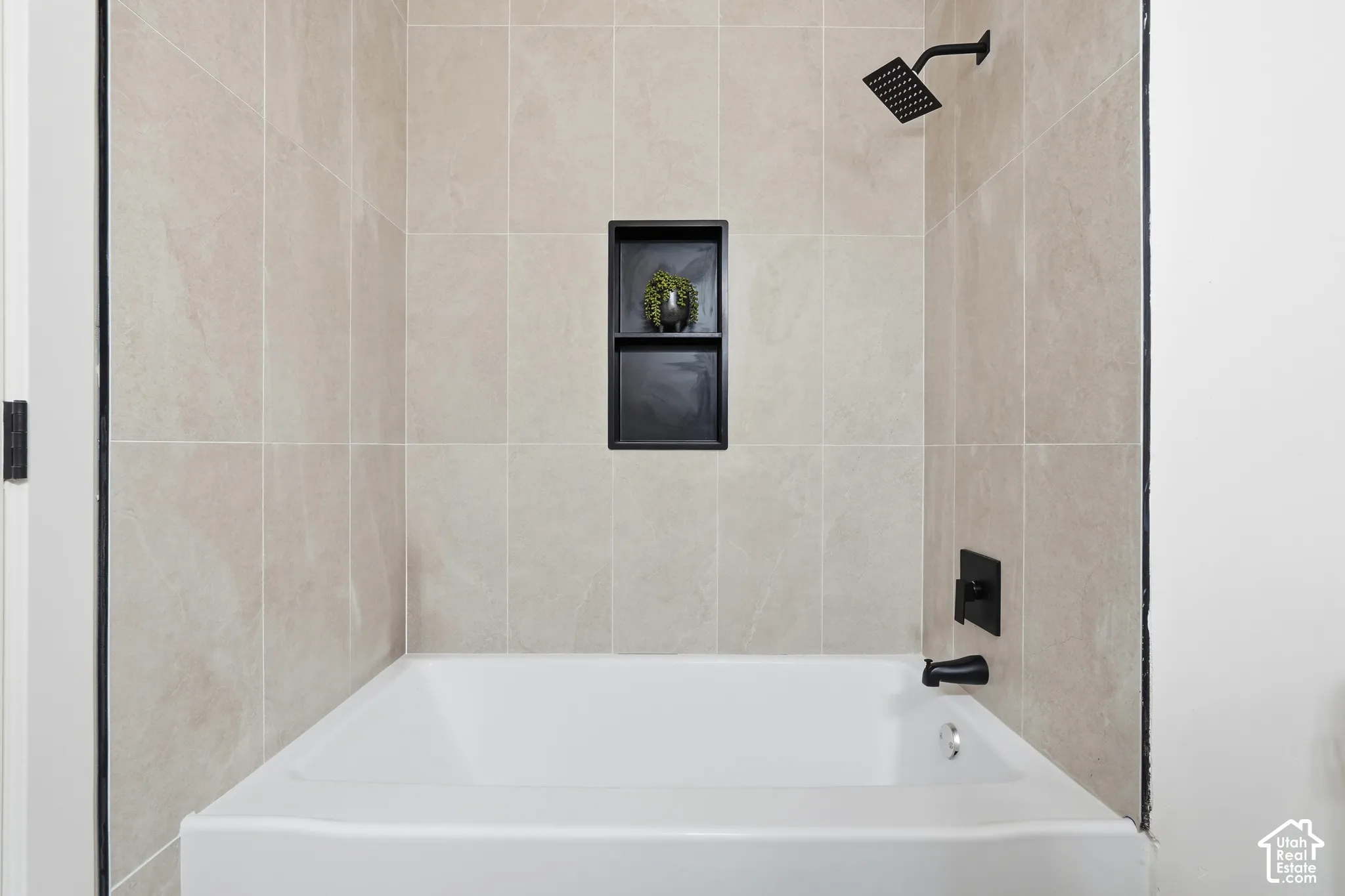 Bathtub with light-toned wall tile, recessed shower niche, matte black showerhead, and matte black tub faucet
