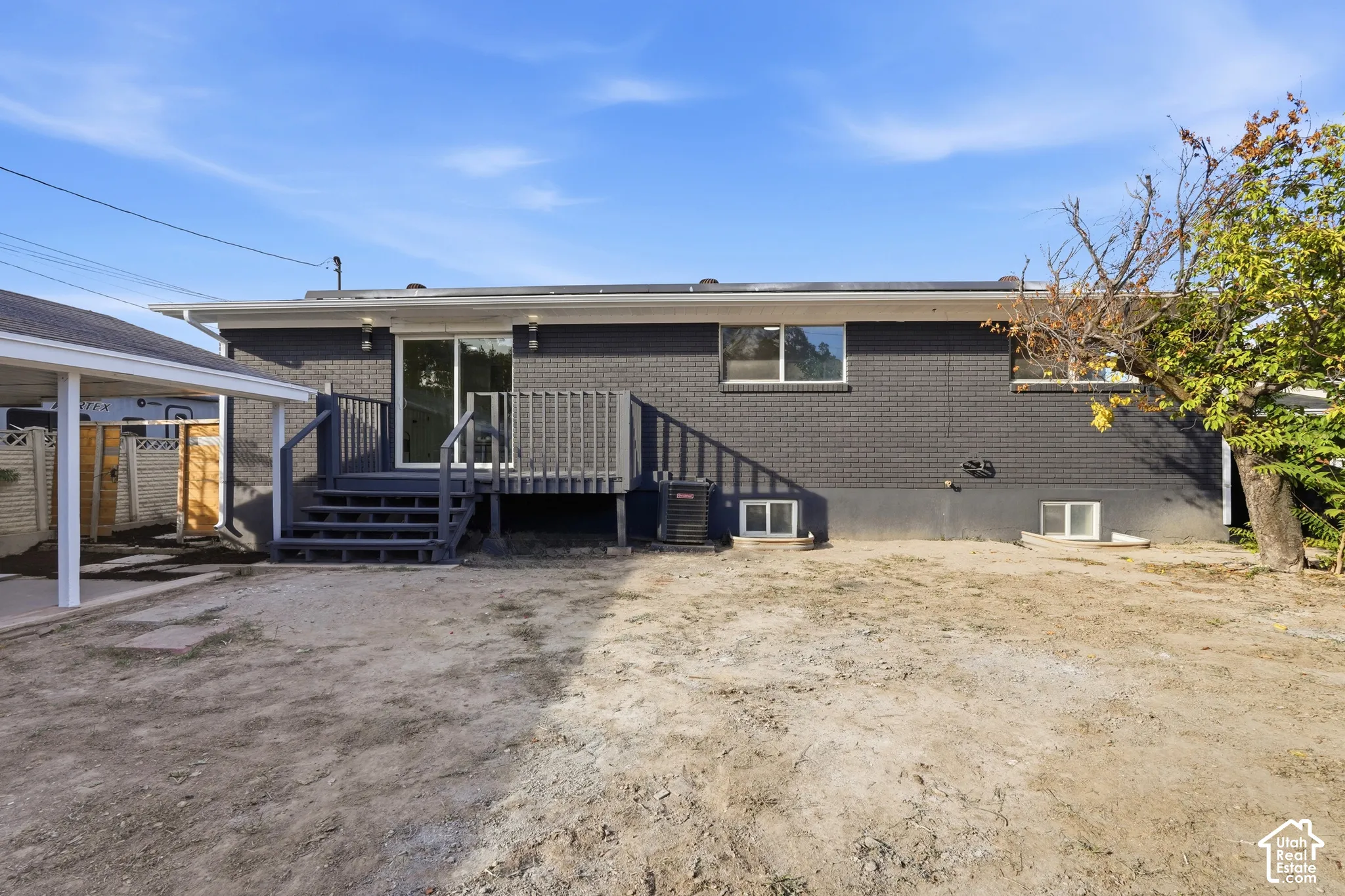 Rear exterior featuring dark brick siding, a raised deck with railing, sliding glass door access, and a covered carport