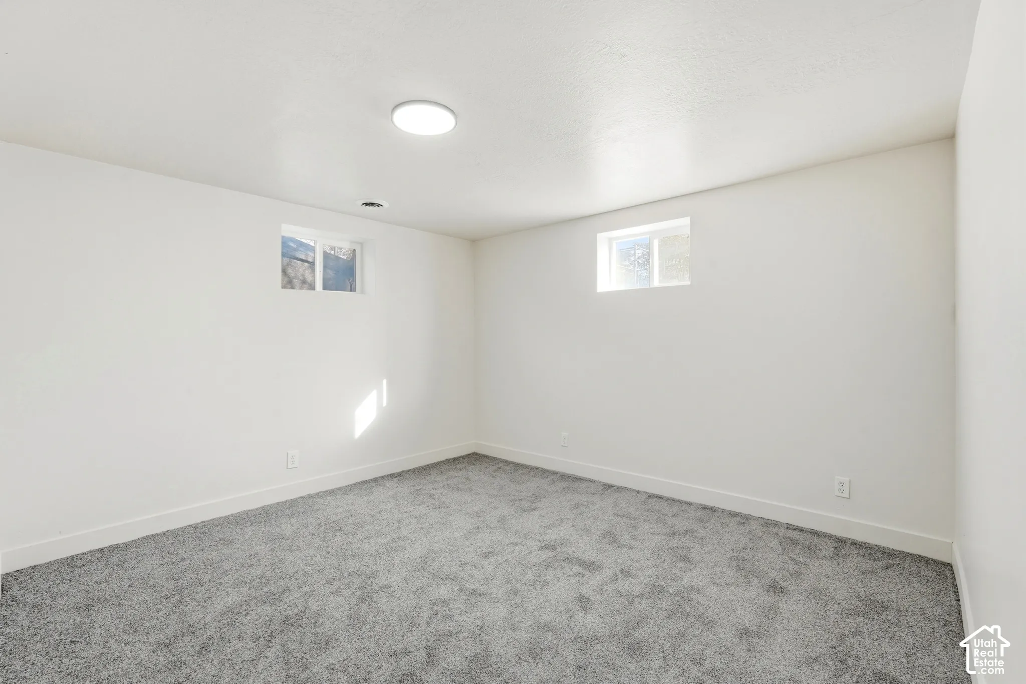 Plush gray carpeting, white walls, two windows, and a ceiling-mounted light fixture