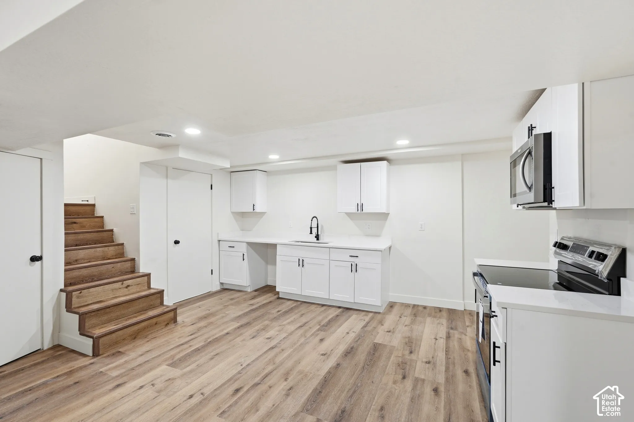 Wood-finish flooring, white cabinetry, integrated microwave, built-in sink, and a black faucet