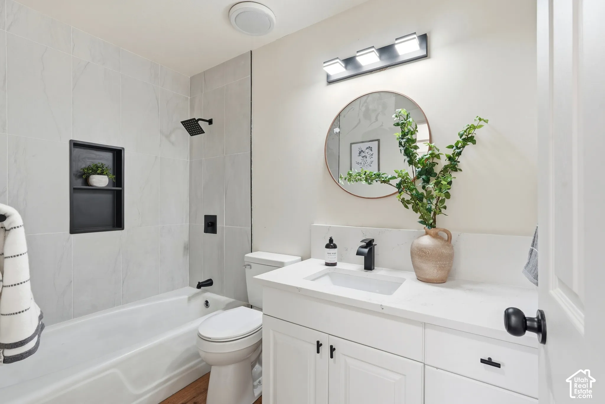 Bathroom featuring a white bathtub, gray tile surround, and a matte black shower fixture