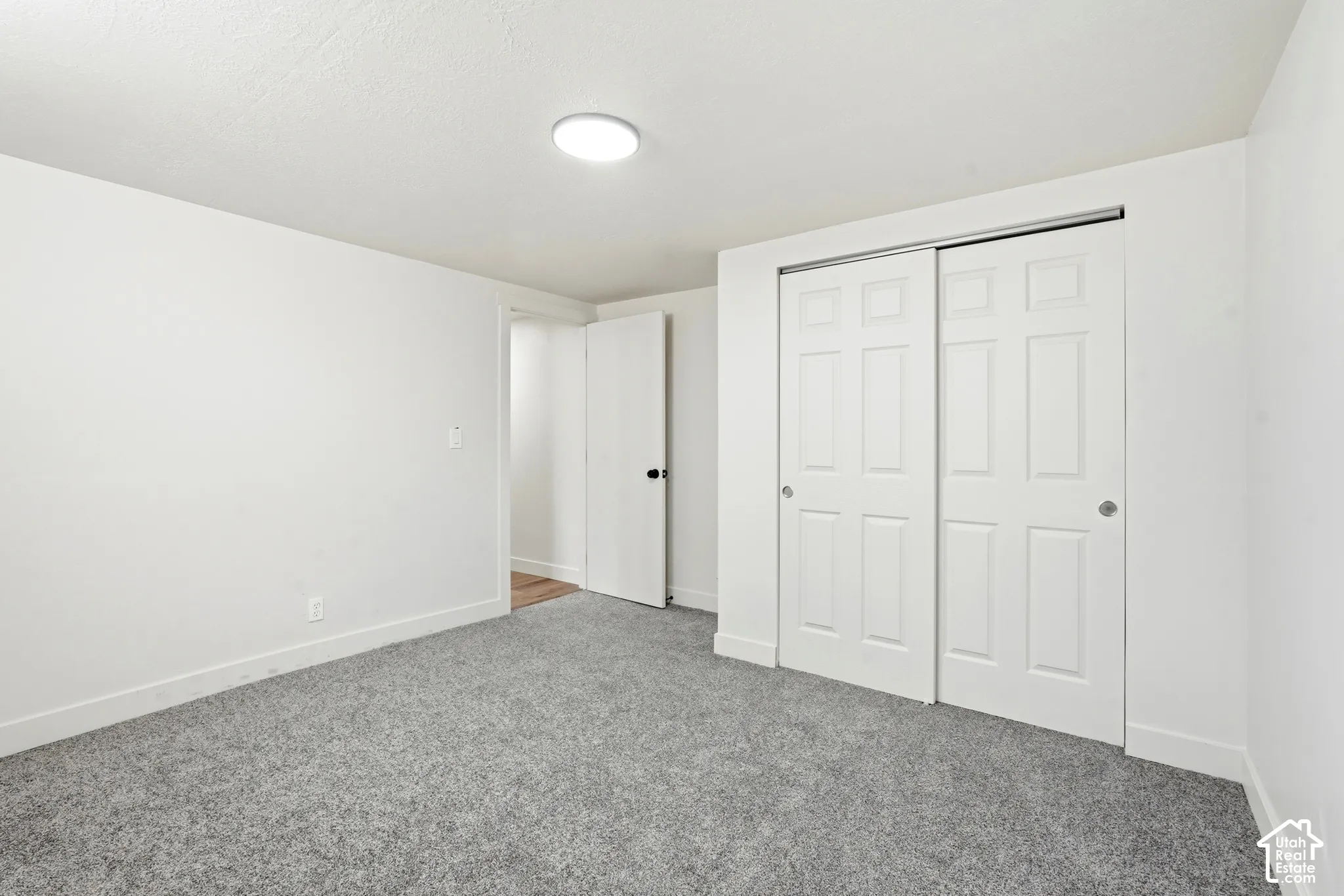 White walls with gray carpeting, featuring a modern flush-mount ceiling light and a two-panel sliding closet door