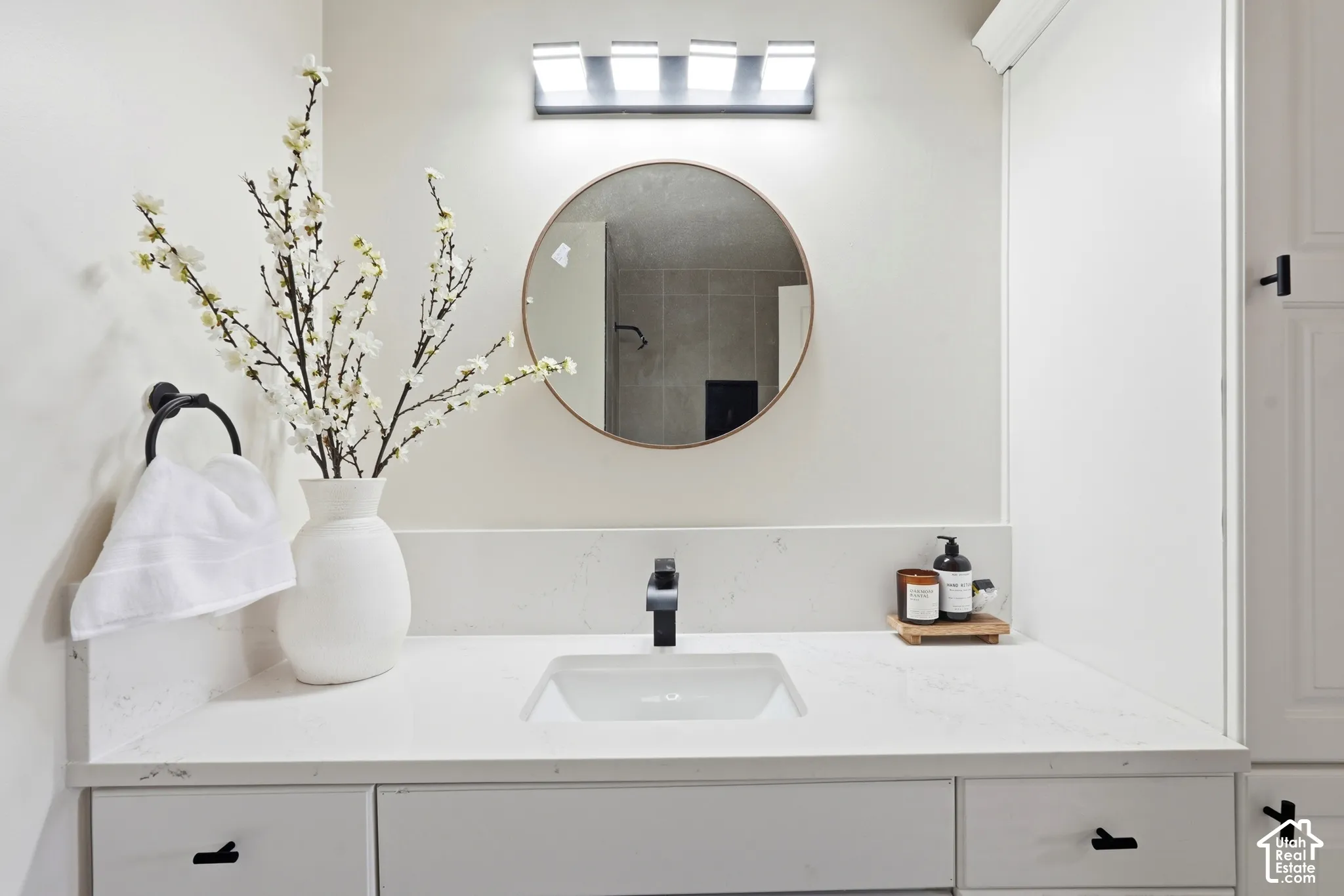 White vanity with an integrated sink, black modern faucet, round mirror, and wall-mounted light fixture