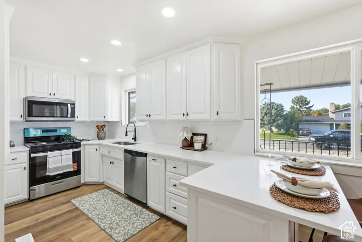 White cabinetry with black hardware, stainless steel appliances, white subway tile backsplash, white countertops, and wood-finish flooring