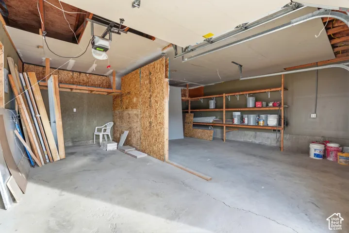 Garage featuring exposed ceiling joists, concrete flooring, built-in shelving, and a garage door opener