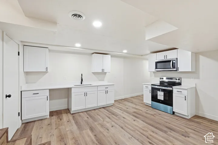 Wood-finish flooring, white cabinetry, integrated sink with matte black faucet, white countertops, and stainless steel microwave